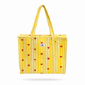 A yellow and white striped tote bag with small red hearts printed all over it, featuring thick braided rope handles and a small white brand label on the front.