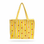 A yellow woven tote bag with vertical white stripes and small red hearts, featuring two braided shoulder straps, shown against a plain white background.
