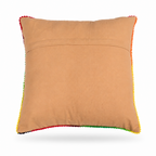 The backside of a square tan throw pillow featuring a vibrant, colorful hand-stitched floral pattern in the center, finished with multicolored pom-pom trim along the edges, shown against a plain white background.