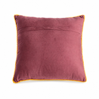The backside of a square throw pillow with a deep plum purple velvet background, featuring colorful embroidered flowers in pink, yellow, blue, and red with green leaves, finished with a yellow pom-pom trim.
