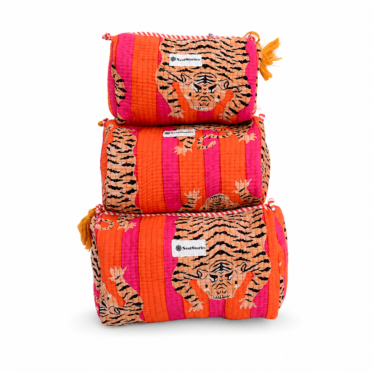 Three stacked quilted canvas cosmetic pouches featuring a vibrant tiger and stripe pattern in orange, pink, black, and beige, with small orange tassels on the zipper pulls. A white brand label reading 'TheBeaute' is visible on each pouch.