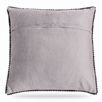 The backside of a square gray throw pillow with black pom-pom trim, featuring a stylized embroidered PUG dog wearing an orange patterned sweater and a colorful floral headband, set against a plain white background.