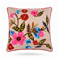A square decorative throw pillow with a beige background and colorful floral embroidery, finished with a red pom-pom trim, shown on a white background.