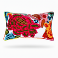 A rectangular decorative throw pillow with a white background and a vibrant, multicolored embroidered floral and animal pattern, featuring colorful pom-pom trim along the edges.
