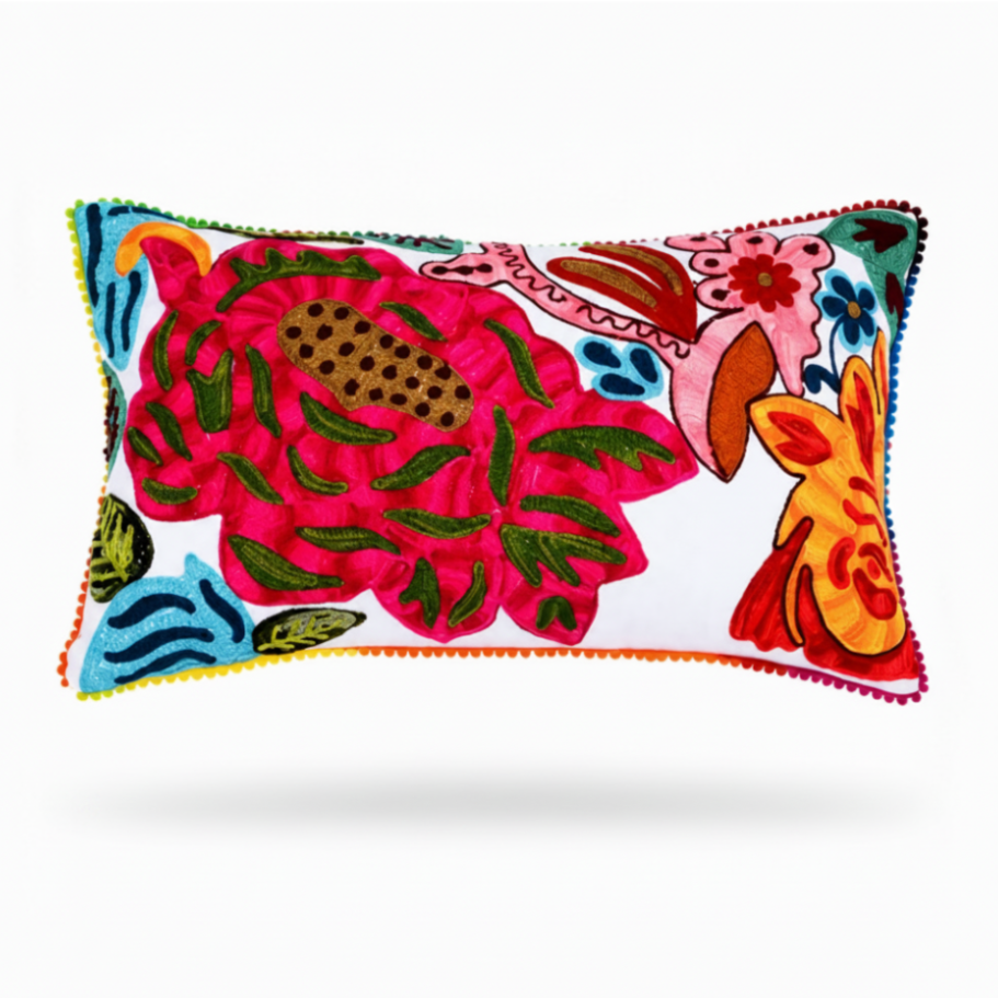 A rectangular decorative throw pillow with a white background and a vibrant, multicolored embroidered floral and animal pattern, featuring colorful pom-pom trim along the edges.