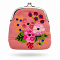 A pink fabric kiss-lock clutch purse featuring a colorful, hand-embroidered floral pattern with green leaves, pink and white flowers, and red and blue accents, set against a plain white background.