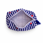 A fabric pouch with a blue and white striped pattern, accented with small red bows and a blue tassel zipper pull, shown open on a white background.