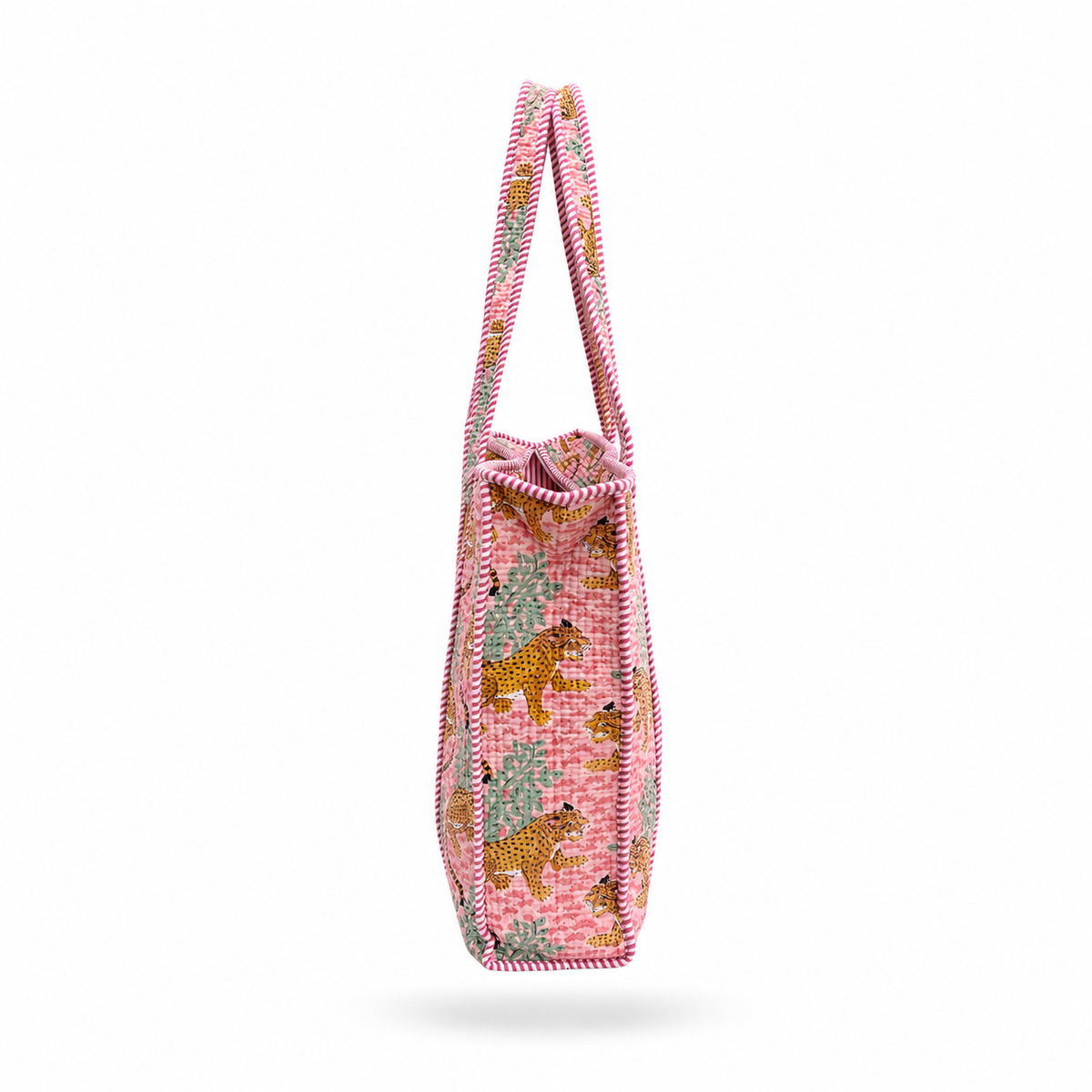 A pink woven tote bag with a pattern of leopards and trees, featuring a pink and white striped handle, shown against a pink white background.