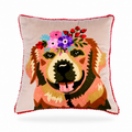 A square decorative throw pillow with a red pom-pom trim, featuring a colorful embroidered golden retriever face with a flower crown on a light beige background.