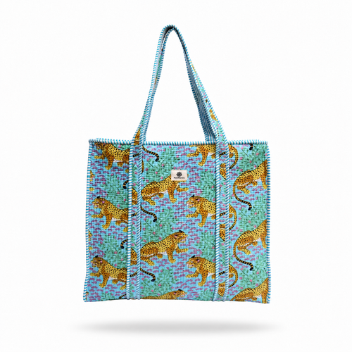 A woven tote bag with a turquoise and purple patterned background, decorated with golden-yellow leopards, featuring two top handles and a small white brand patch on the front.