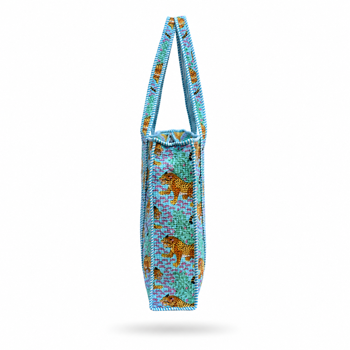 A Tote bag featuring a pattern of golden leopards on a turquoise and purple background, with light blue braided shoulder straps, shown against a plain blue purple background. 