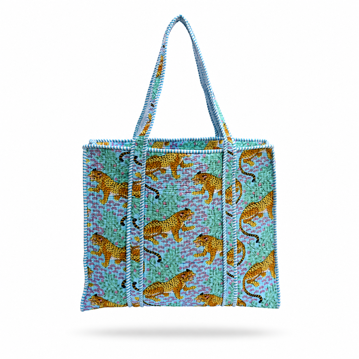 A Tote bag featuring a pattern of golden leopards on a turquoise and purple background, with light blue braided shoulder straps, shown against a plain blue purple background. 
