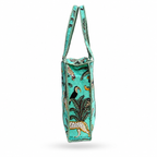 a side view of a  turquoise tote bag with a tropical print featuring palm trees, toucans, zebras, and birds, finished with black and turquoise braided handles and trim, shown on a white background.