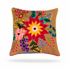 A square tan throw pillow featuring a vibrant, colorful hand-embroidered floral pattern with pom-pom trim on a white background.